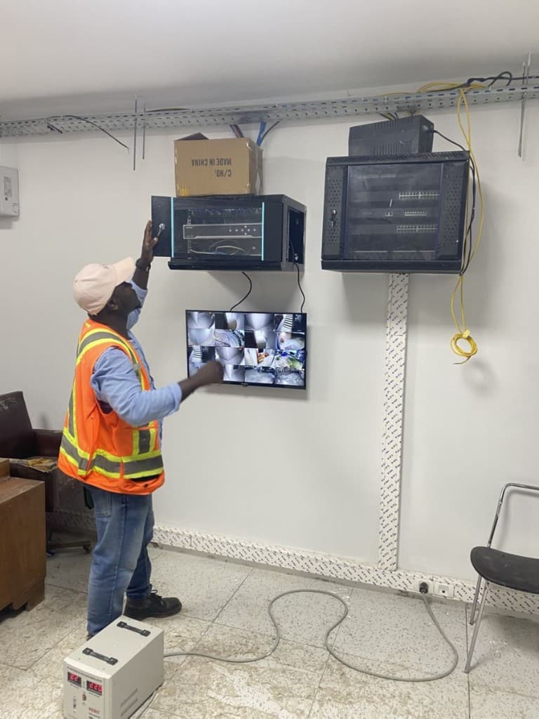 Technician installing wall-mounted network racks above a multi-camera monitoring screen